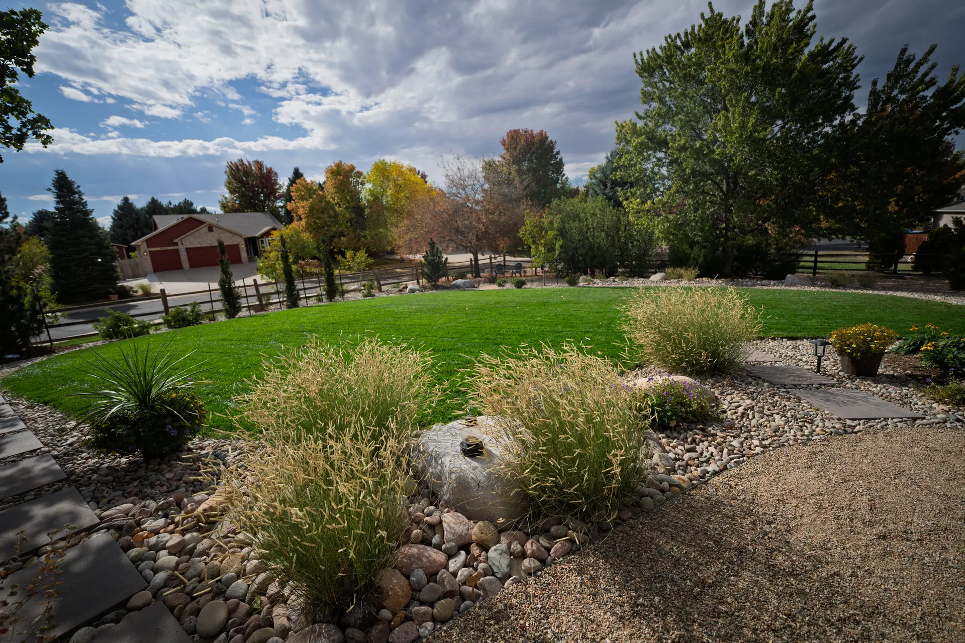 Frederick, Colorado Backyard xeriscape with river rock beds, native ornamental grasses, a boulder, and stepping stones bordering a curved green lawn",Xeriscape Backyard with River Rock and Ornamental Grasses,"Water-wise backyard: river rock beds, native grasses, and a curved lawn edge.","Backyard xeriscape renovation in Colorado by The Landscape Company. River rock planting beds with native ornamental grasses, a feature boulder, stepping stones, and path lighting frame a curved lawn.